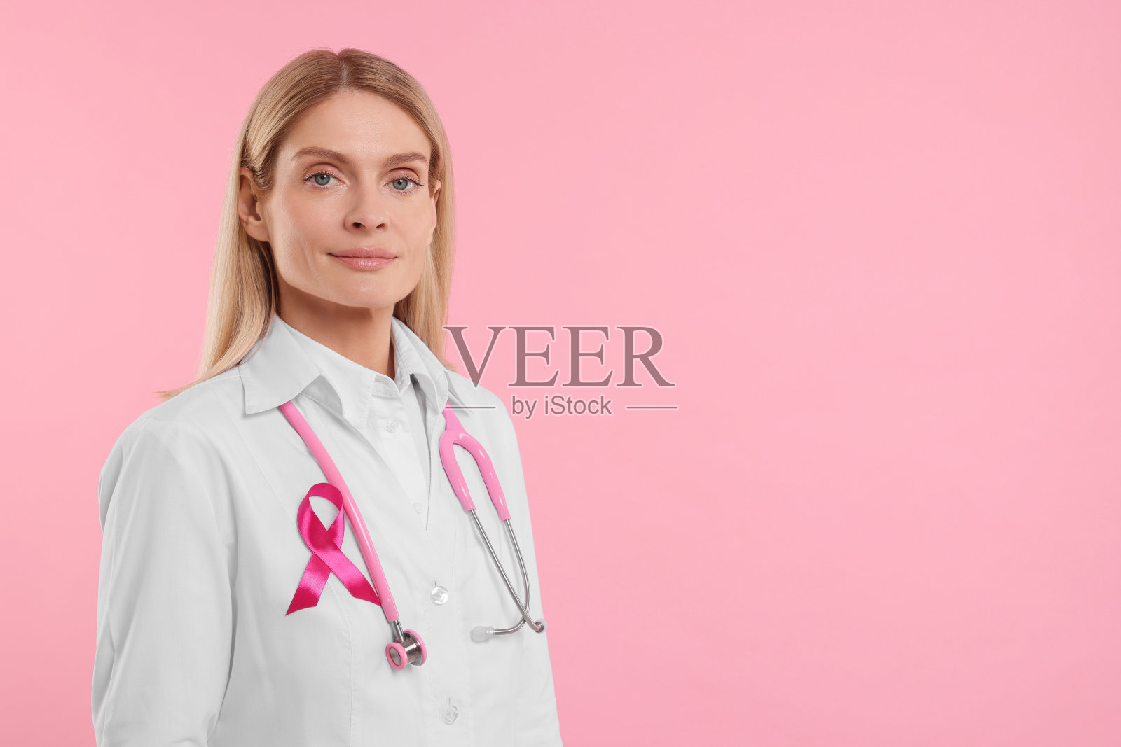 医生与粉红色丝带和听诊器在彩色背景，文字的空间。乳腺癌意识照片摄影图片