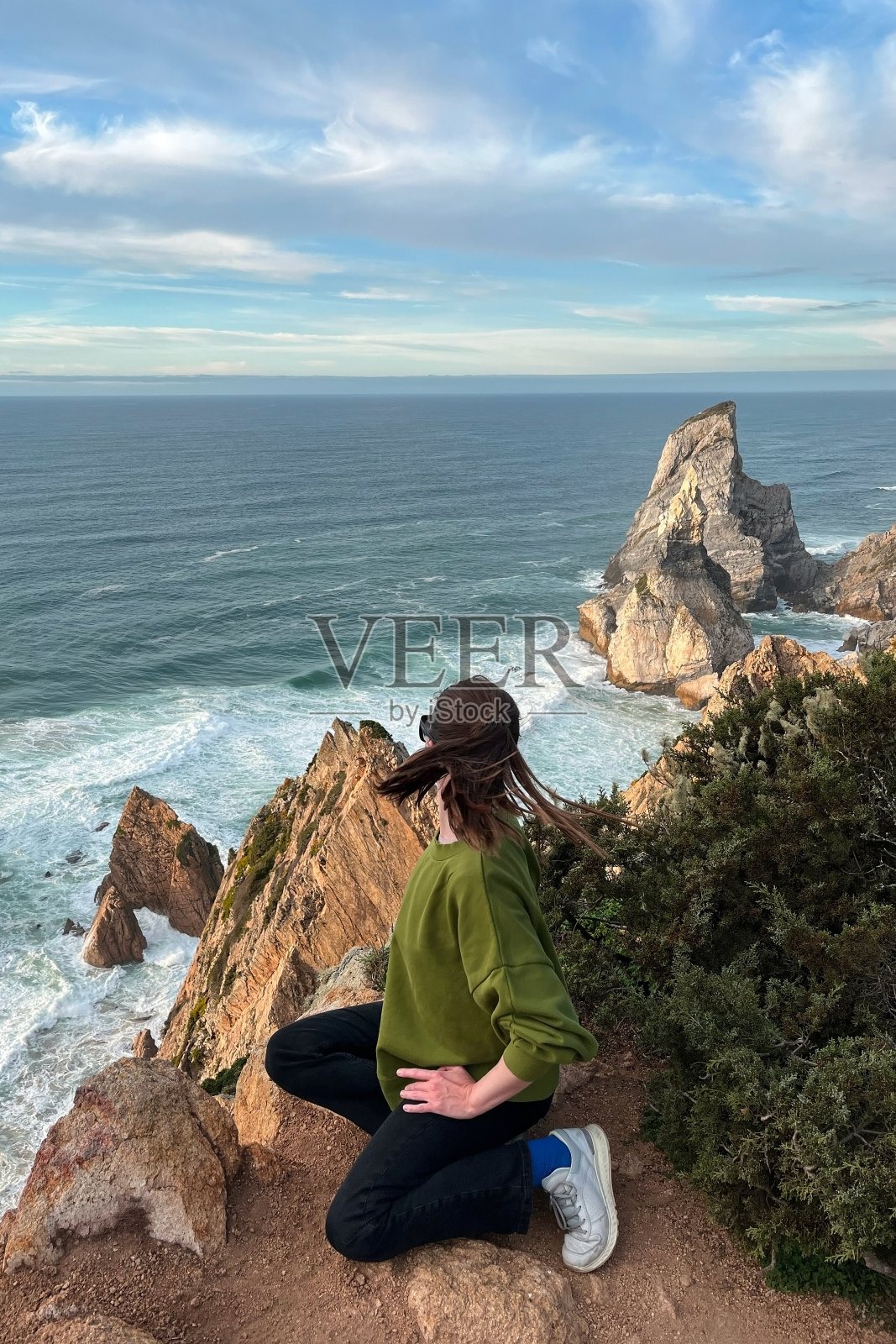 年轻女子坐在悬崖上，看着葡萄牙的大西洋照片摄影图片