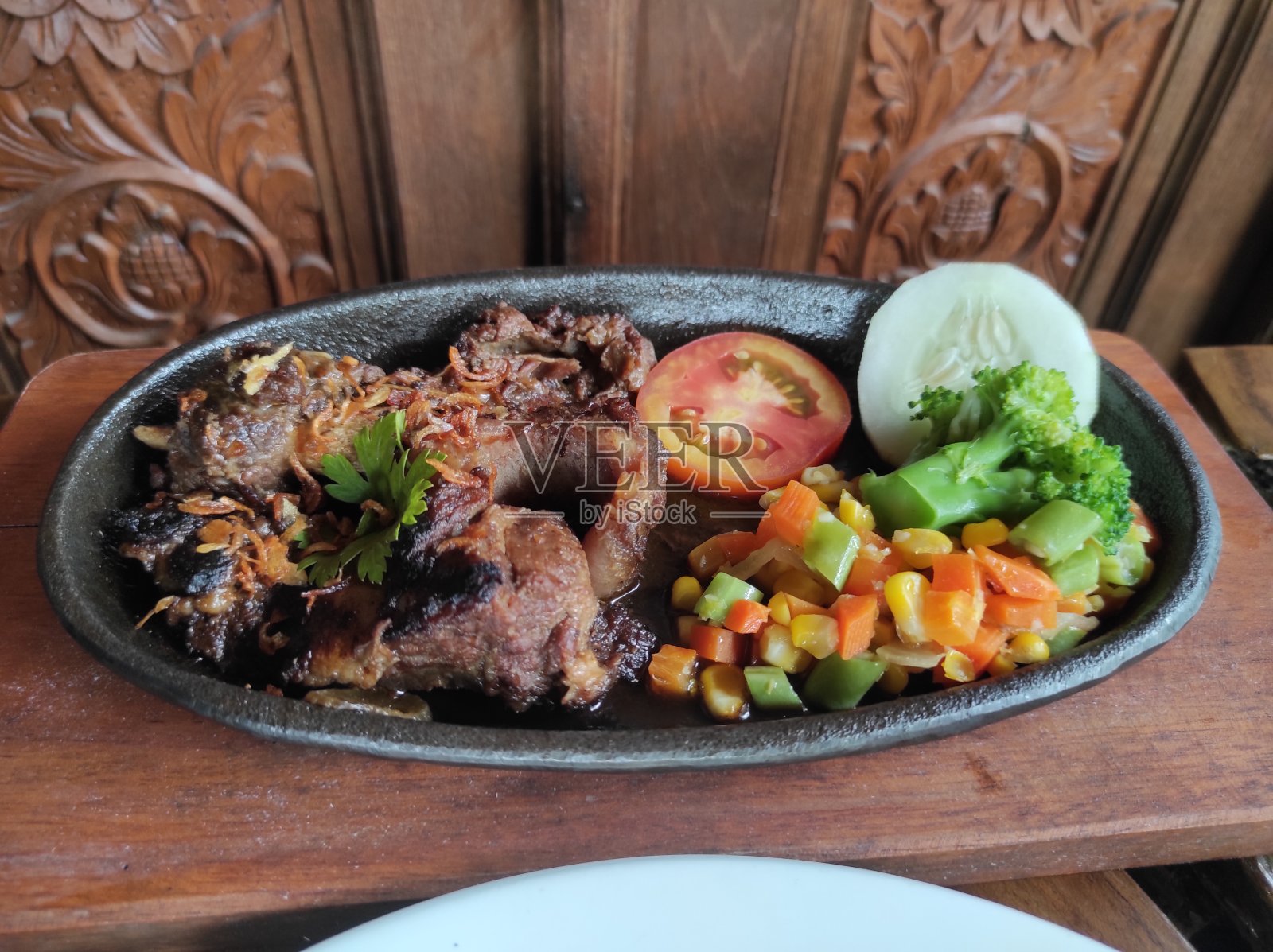 美味的烤排骨，放在热盘子上，配上西红柿、黄瓜、玉米片和胡萝卜照片摄影图片