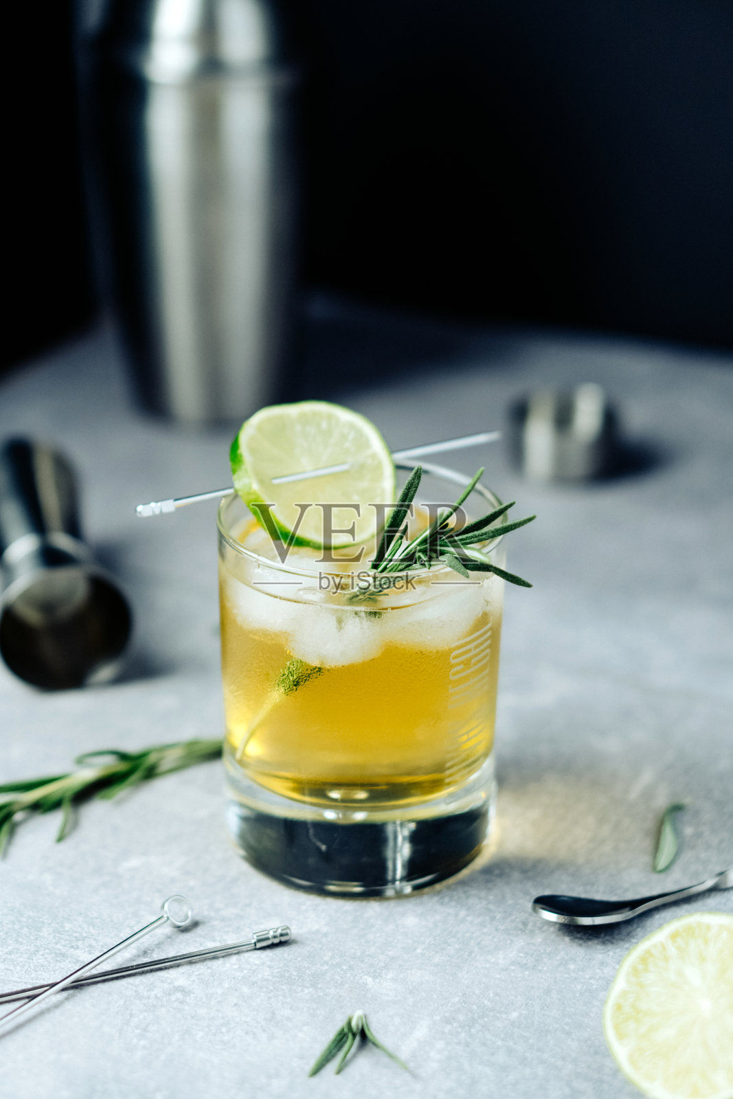 酒精鸡尾酒，柠檬片迷迭香冰和鸡尾酒摇酒器，黑色背景。派对时间照片摄影图片