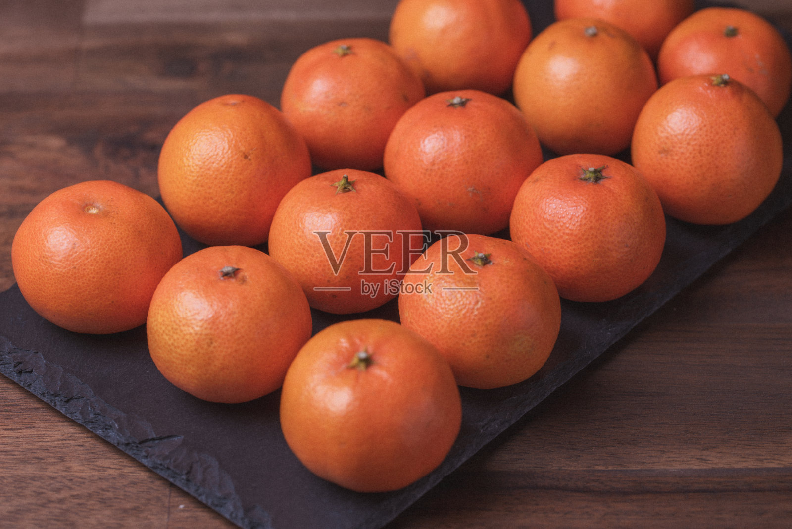 水果。照片中的橘子在黑色的石板上一字排开。照片摄影图片
