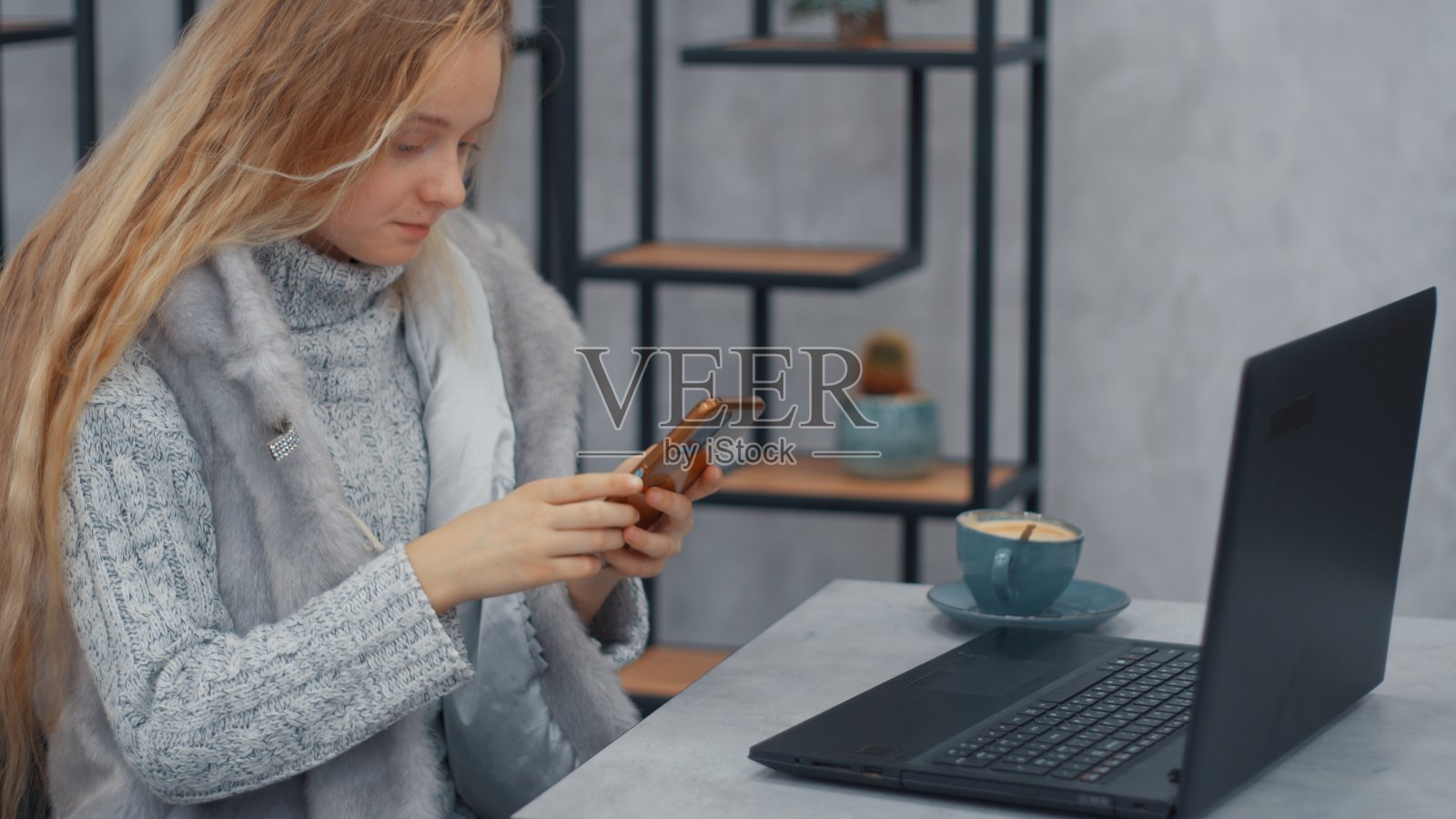 长发少年坐在笔记本电脑前看手机照片摄影图片