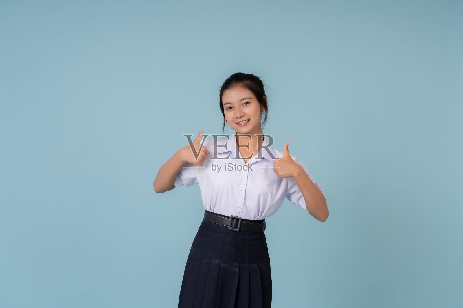 亚洲女高中生竖起大拇指的标志非常好用于展示网站或海报。辅导机构教育主持人在蓝色背景的摄影棚里拍照照片摄影图片