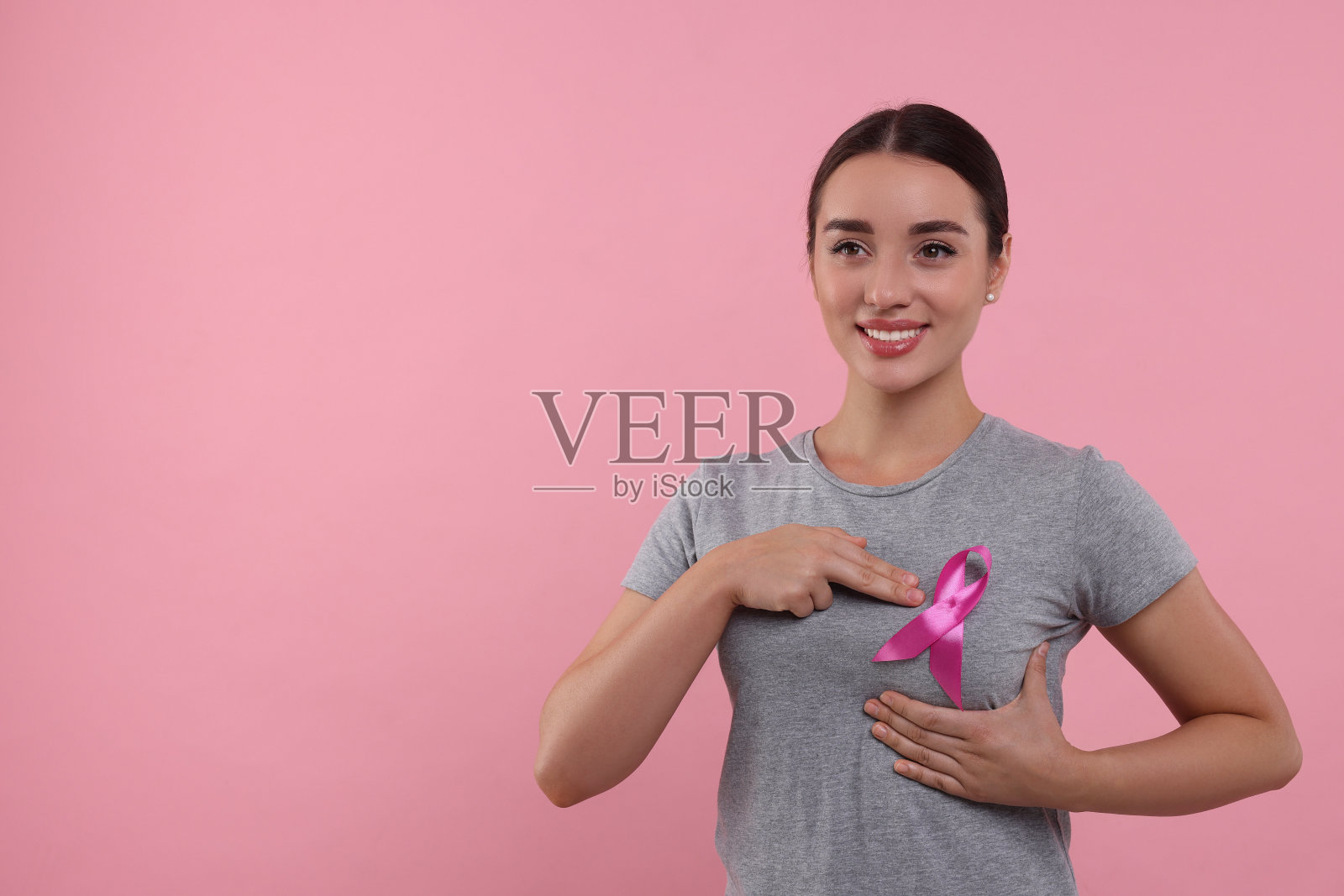美丽的年轻女子与粉红色丝带的彩色背景，文字的空间。乳腺癌意识照片摄影图片