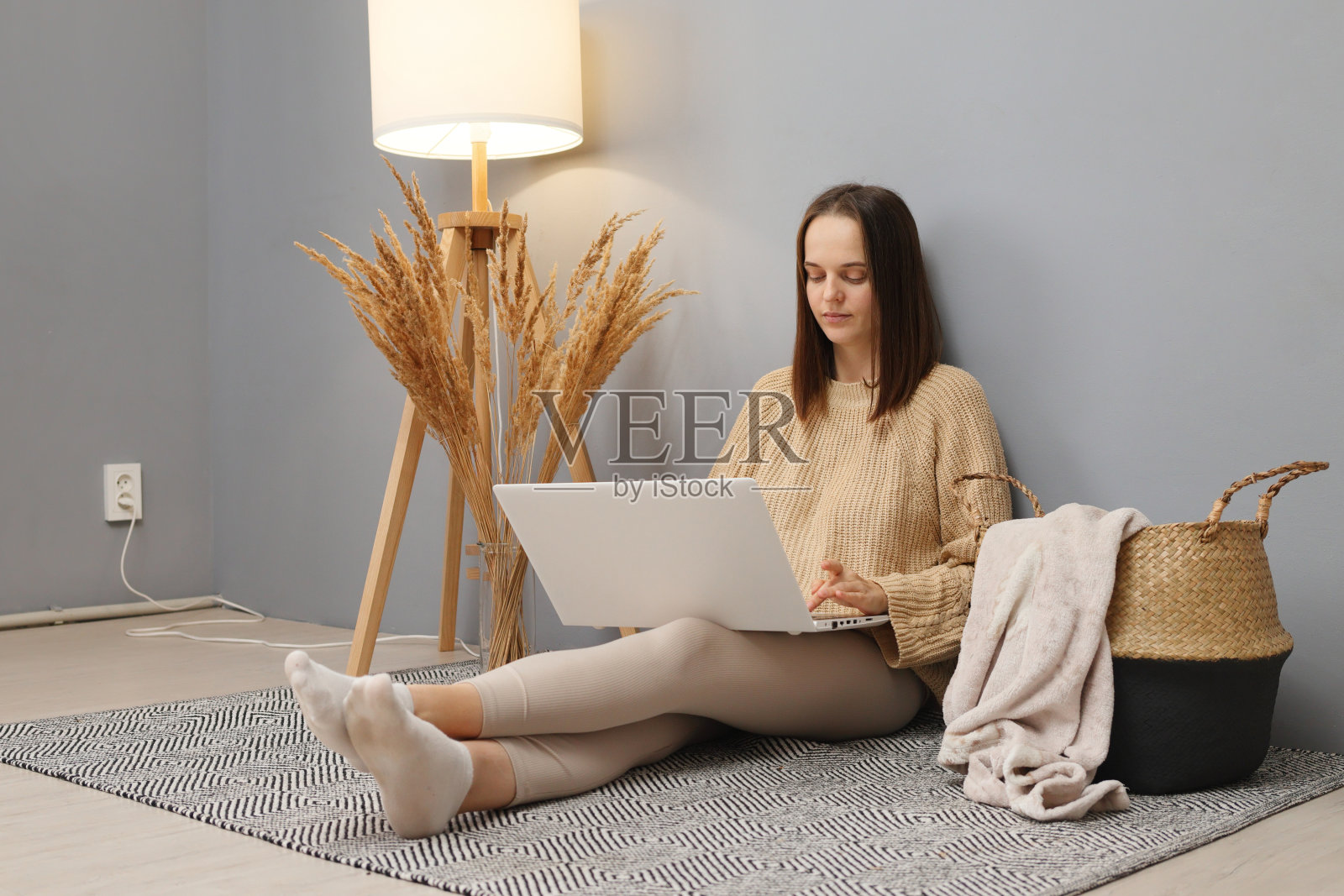 基于互联网的自由职业者。经理的数字任务。穿着米色套头衫的白人女性坐在灯光明亮的房间地板上，用键盘打字照片摄影图片