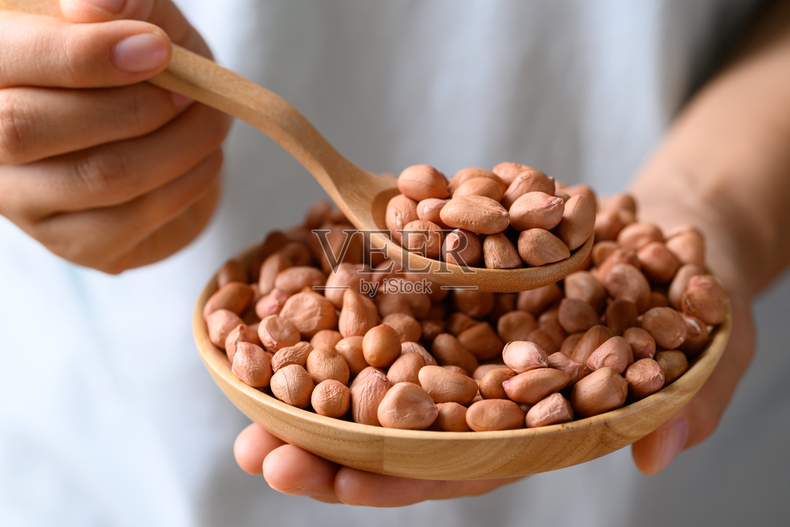 花生装在木碗里，用手拿着勺子照片摄影图片