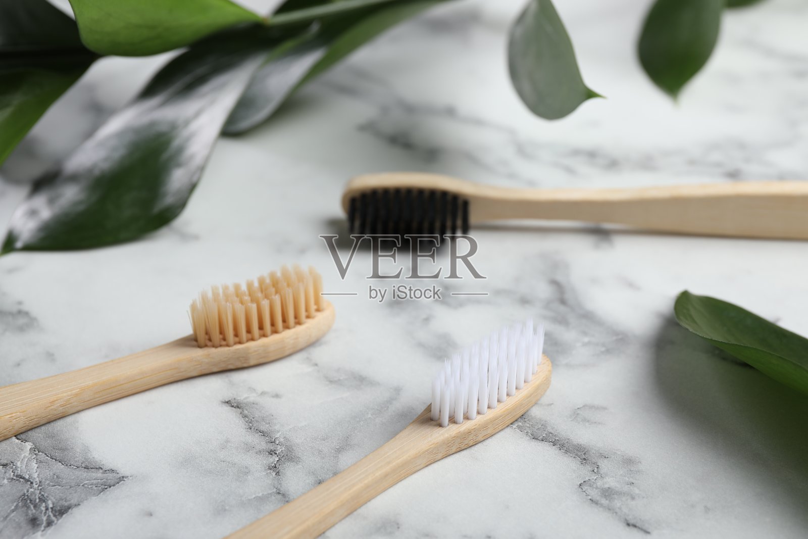 白色大理石桌子上的竹牙刷和绿叶，特写照片摄影图片