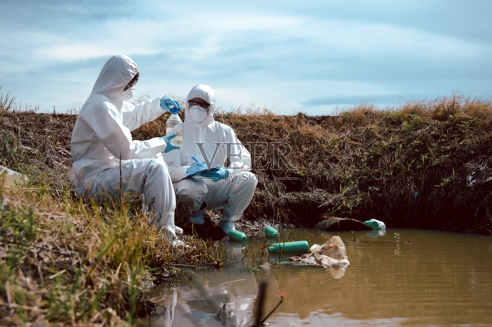 一队科学家或生物学家穿着防护服，用装满化学物质的垃圾瓶子从天然水源采集水样。水污染概念。照片摄影图片