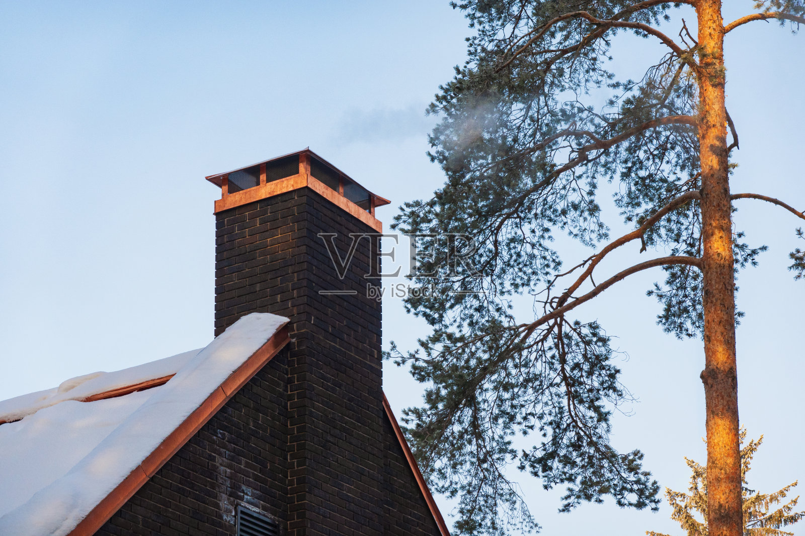 在一个霜冻的日子里，轻烟从砖房的烟囱里升起。有雪，有天空，有松树。照片摄影图片