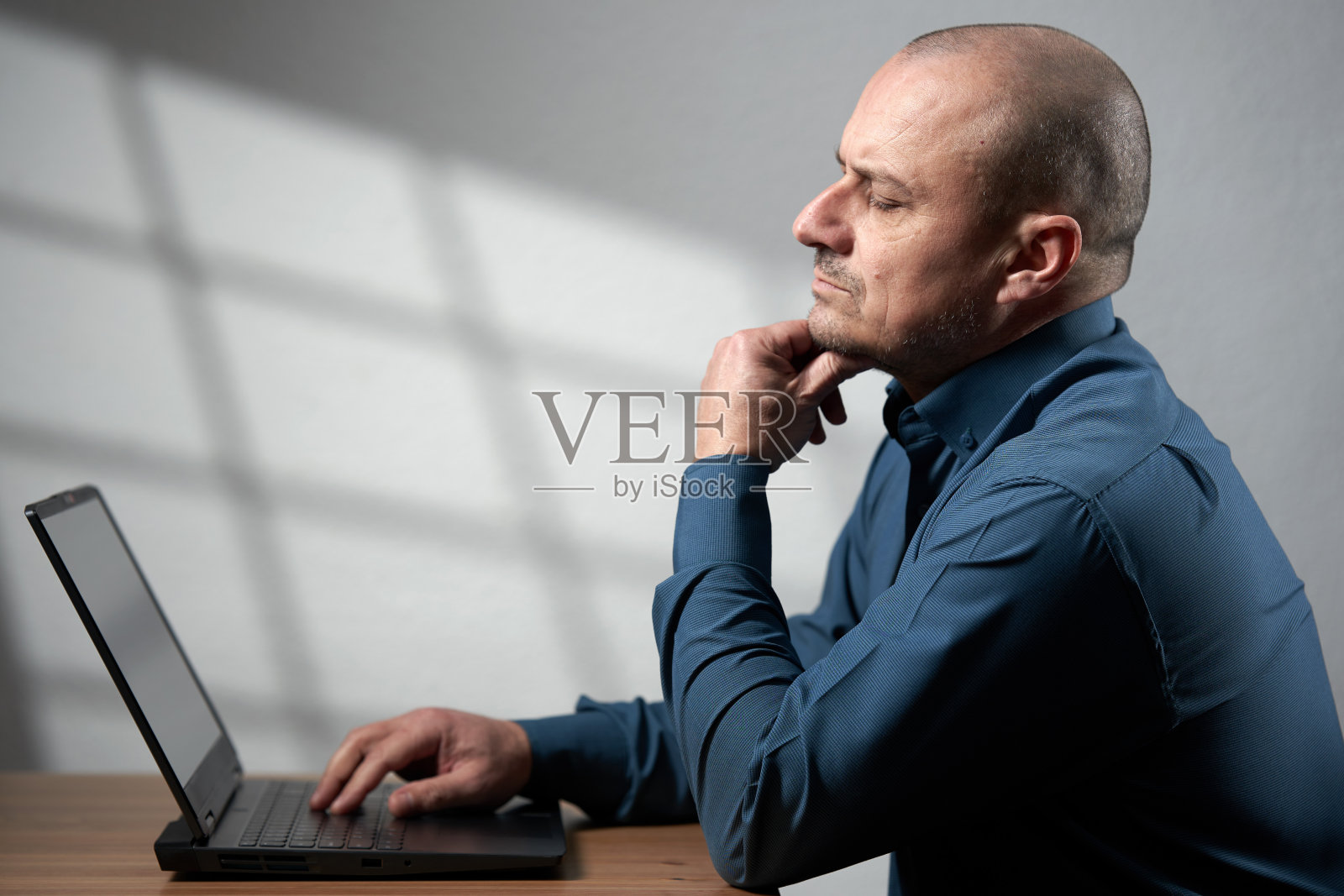 成熟的商人，桌上放着笔记本电脑，沉思着照片摄影图片