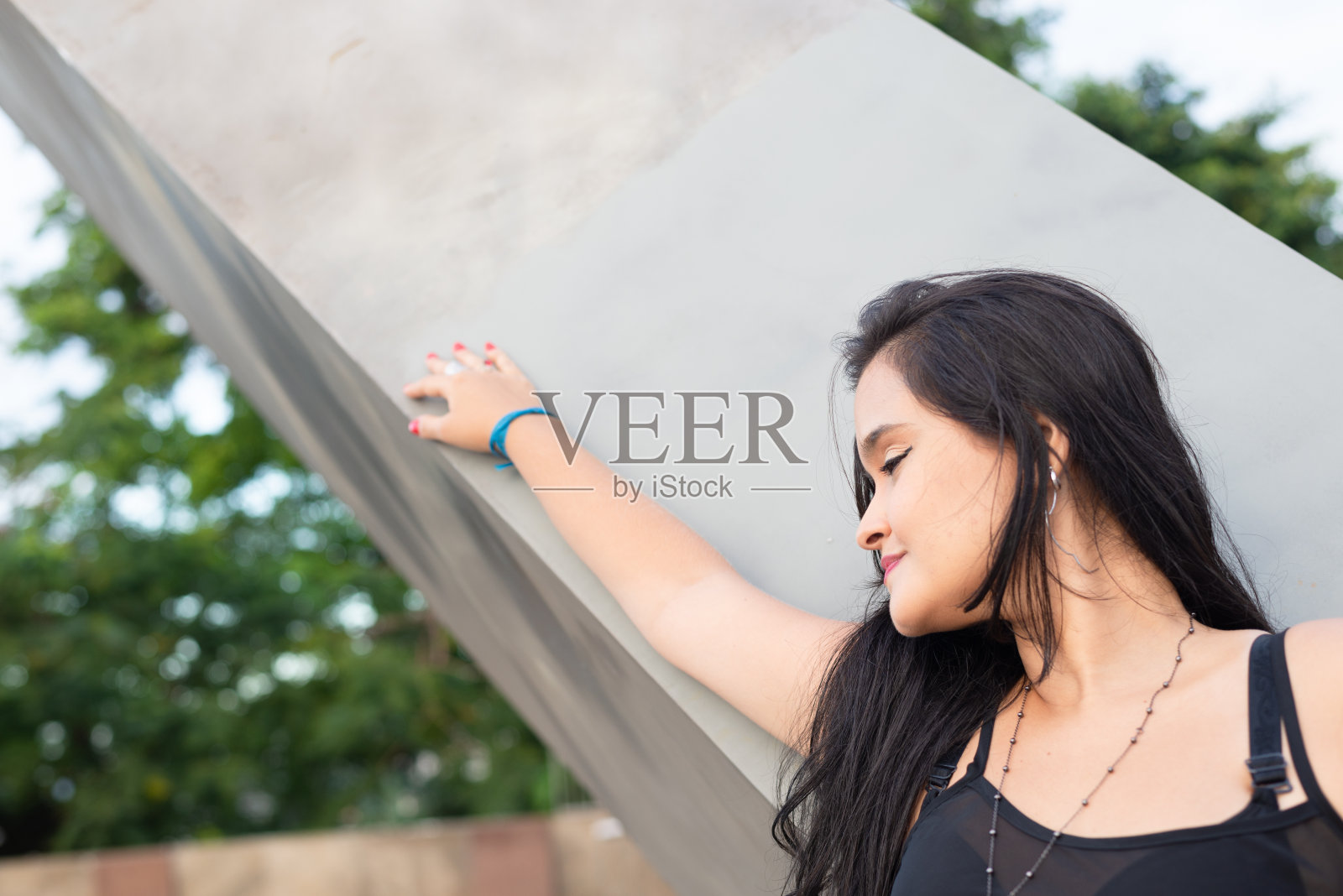 一个漂亮的黑发女人靠在水泥柱上的上半身。照片摄影图片