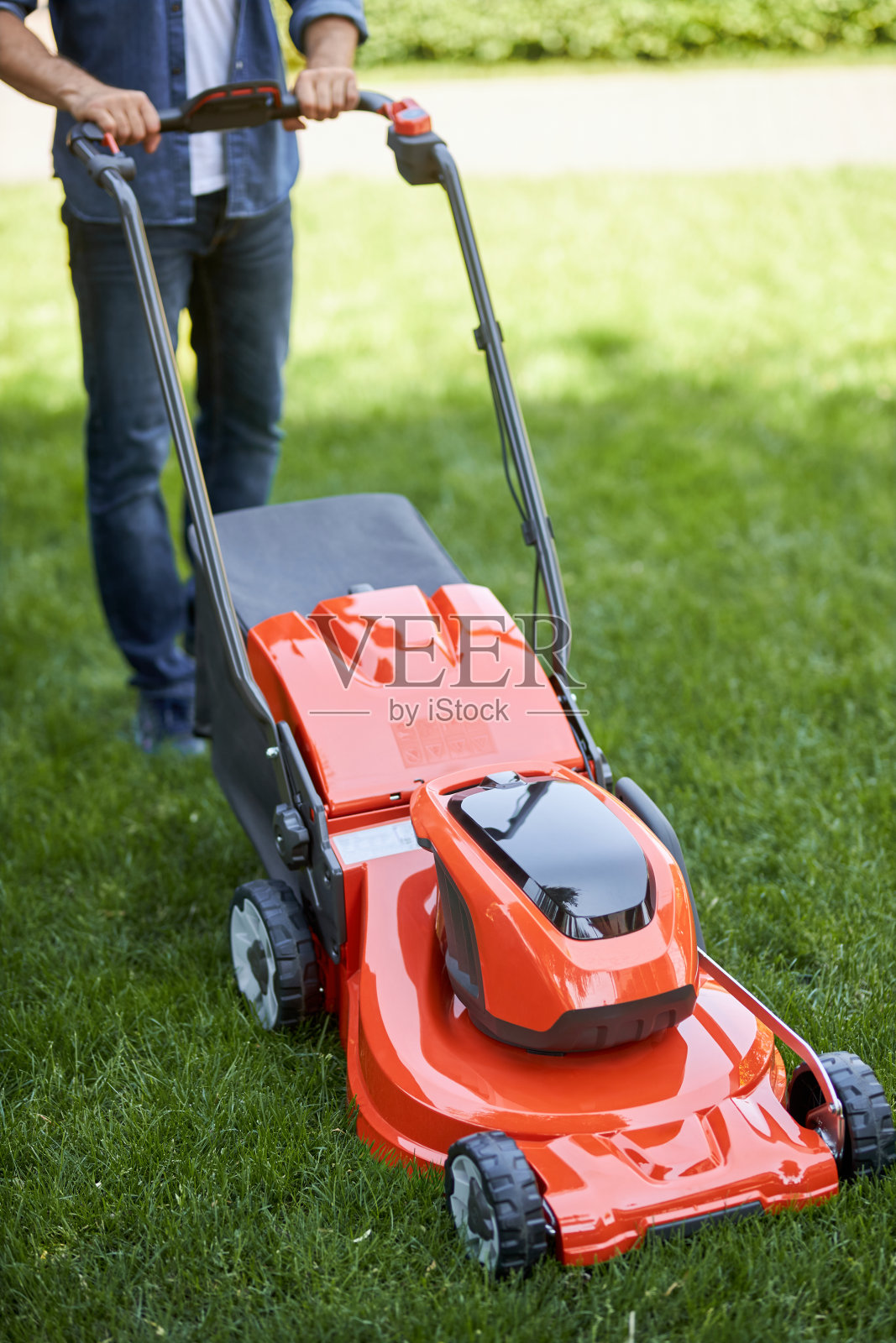 不知名的男性工人在外面用现代的橙色割草机割草。照片摄影图片