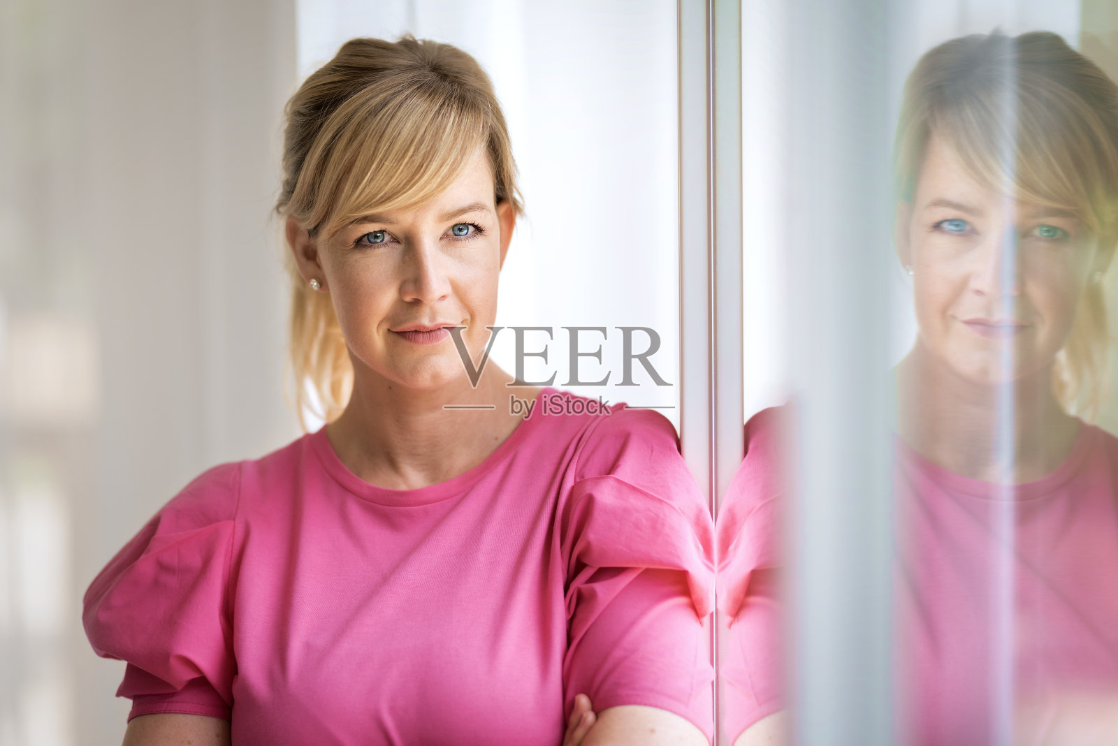 漂亮的金发女人站在家里的窗边做白日梦照片摄影图片