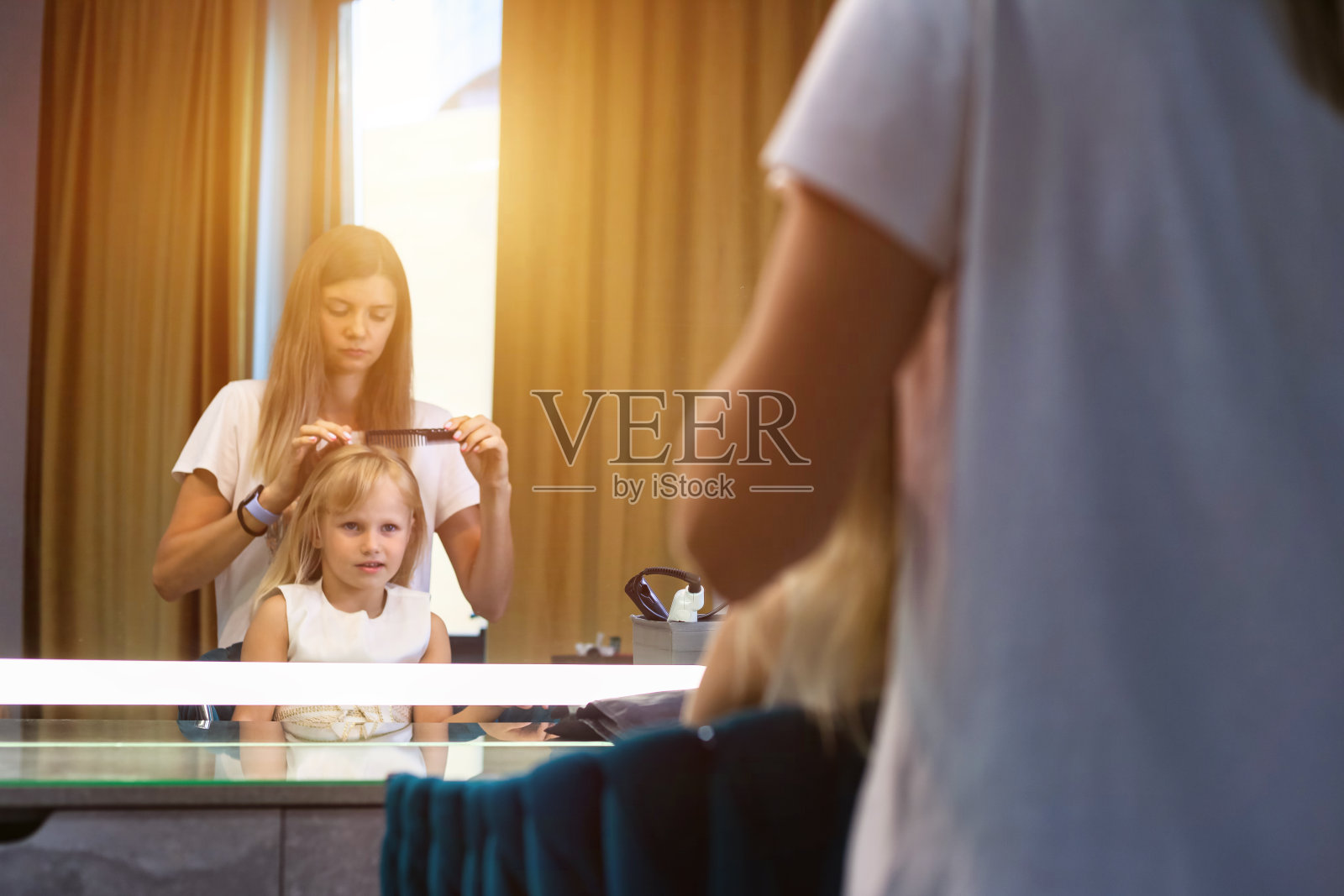 理发店，女理发师在镜子前为理发店里的女孩梳头，护发。美发师女士用梳子为孩子做卷发。美发沙龙的客户服务概念。复制广告文本空间照片摄影图片