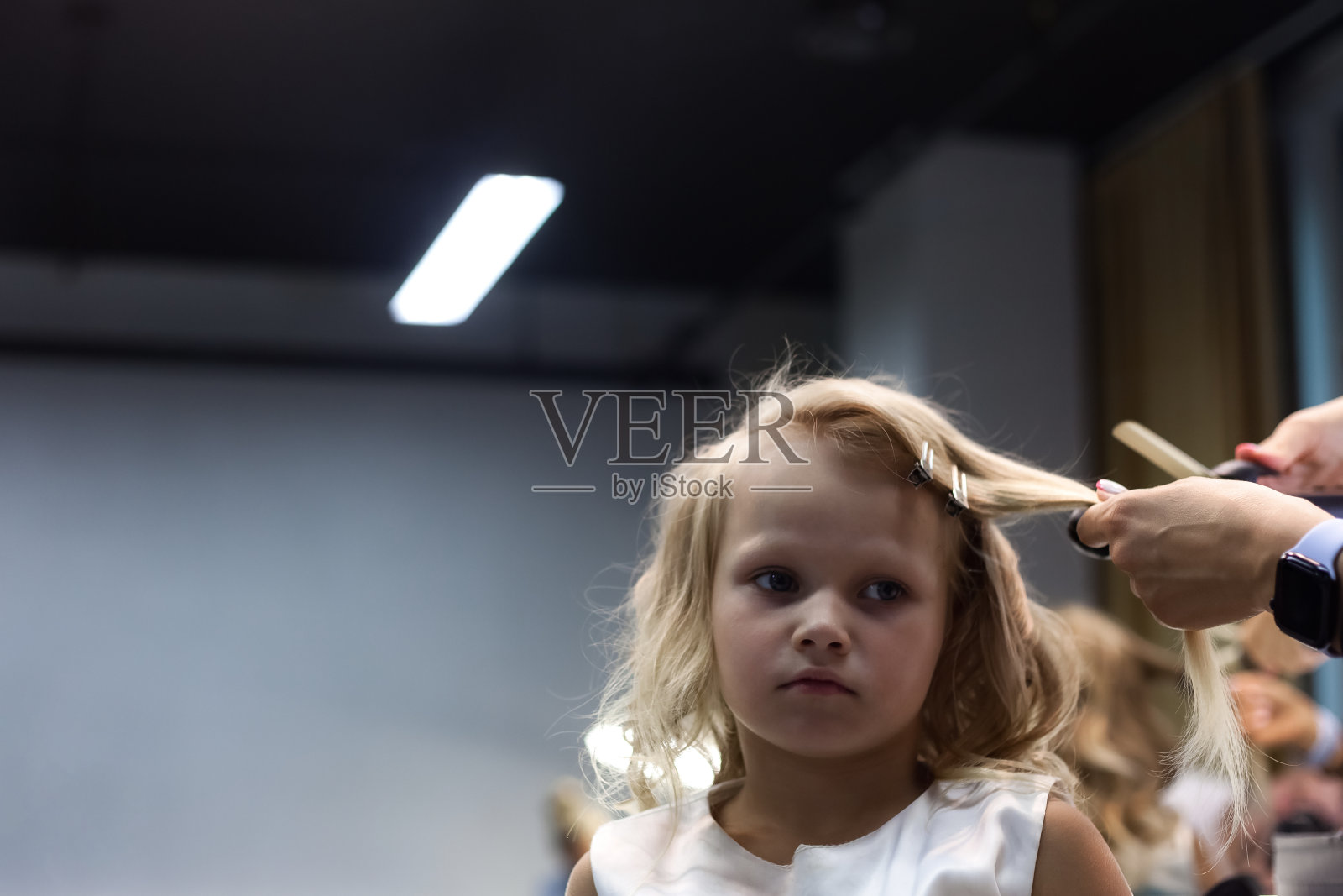 美发师在理发店为可爱的女孩做卷发。理发师女士在镜子前为可爱的孩子做卷发，护发。美发沙龙的客户服务概念。复制广告文本空间照片摄影图片