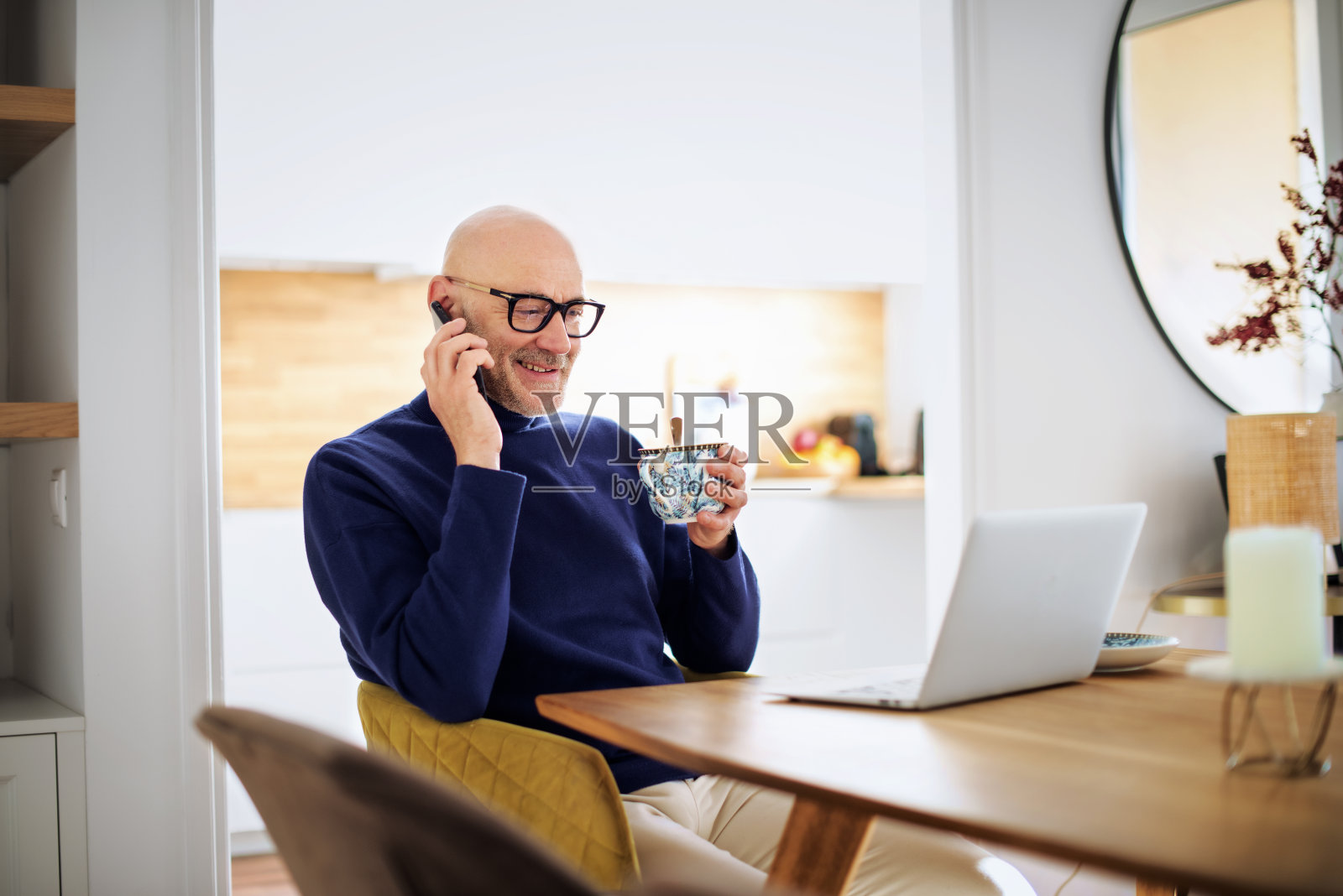 一个成熟的男人在家里打电话，一边工作一边使用笔记本电脑照片摄影图片