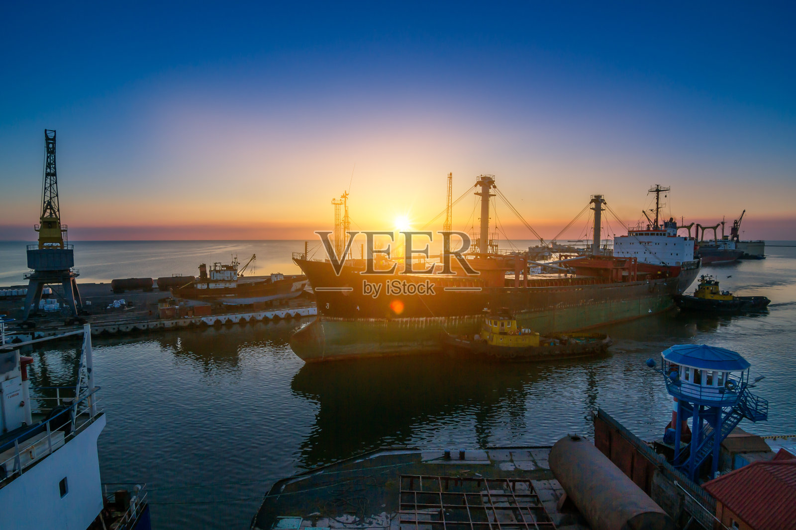 日出的海港熙熙攘攘，货船停靠在泊位上，起重机准备卸货。全球贸易物流中心，货机随时准备国际交货。清晨的工业海运码头。照片摄影图片