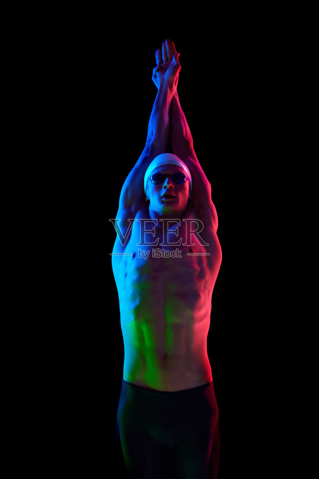 运动的年轻人，游泳运动员，肌肉发达，强壮，宽松的身体戴着帽子和护目镜，在霓虹灯的黑色背景下展示游泳技术照片摄影图片