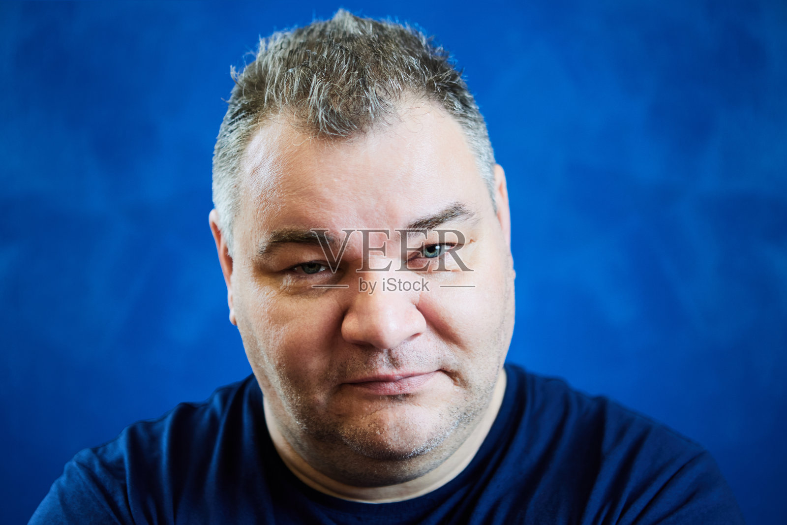 一位47岁的欧洲男子，在蓝色的背景下，微微低下头，用锐利的目光凝视着。照片摄影图片