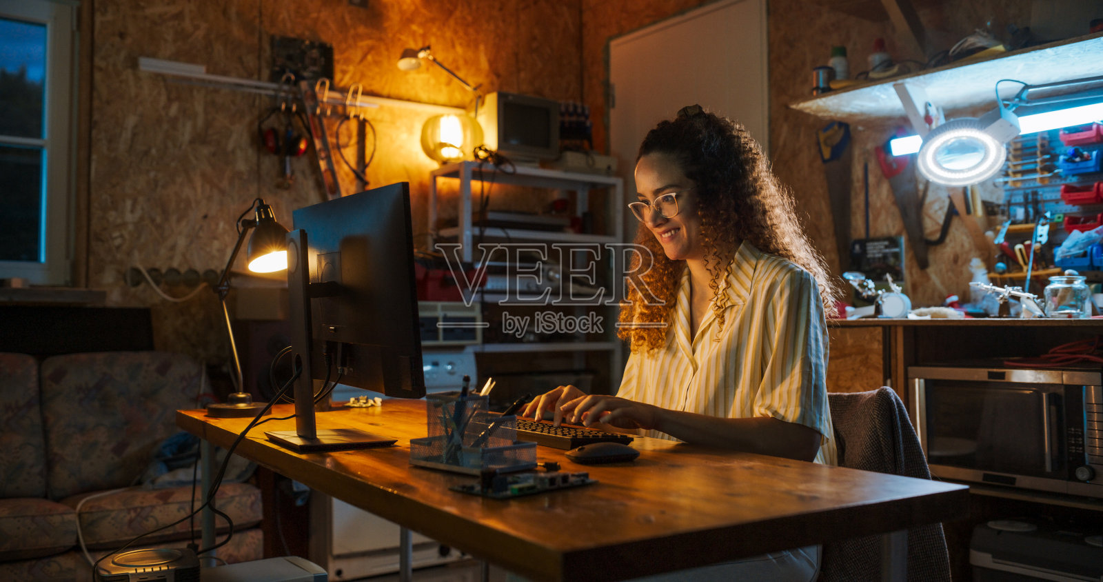 西班牙裔女性软件工程师深夜在复古车库的台式电脑上编程的肖像。雄心勃勃的女性创办科技创业公司。在家编码创新的在线服务。照片摄影图片