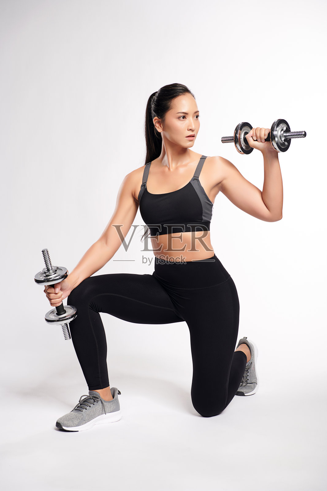 一位亚洲女性穿着白色背景的运动运动服，举着哑铃健身。照片摄影图片