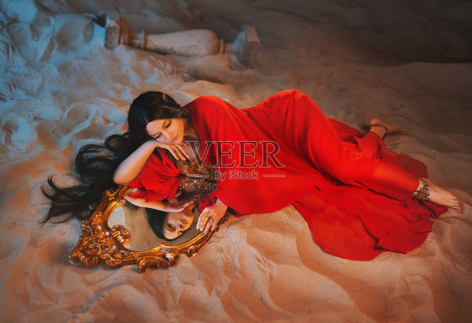艺术肖像真实幻想女孩阿拉伯女人仙女女王看着镜子中的反射魔法。美丽的女孩躺在满是沙子的房间里。红色长裙梦脸仙女风格夜月光阿联酋迪拜照片摄影图片