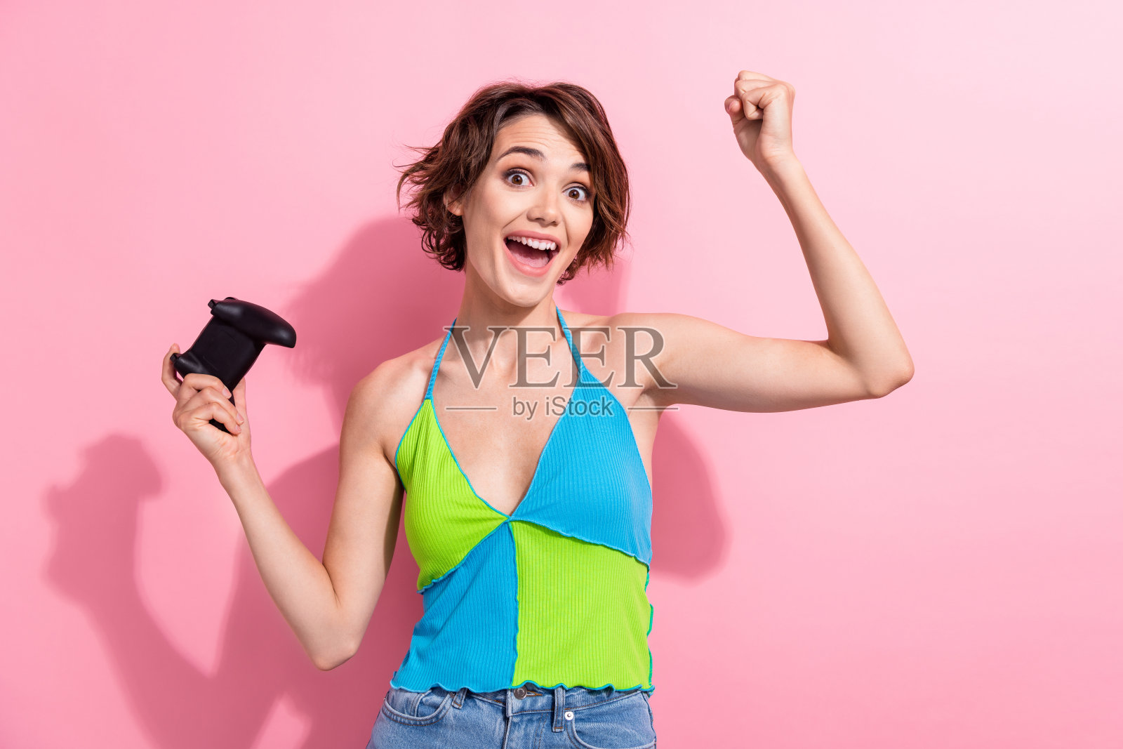 迷人的沉迷游戏的年轻女子的照片举起拳头度过她的暑假玩控制台孤立的粉红色背景照片摄影图片