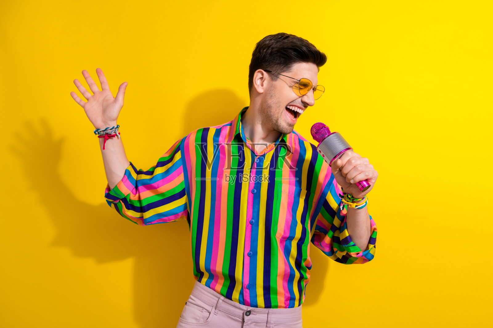 疯狂的年轻人对着粉色麦克风唱歌，专业歌手在公司活动中为员工演唱，背景是黄色照片摄影图片