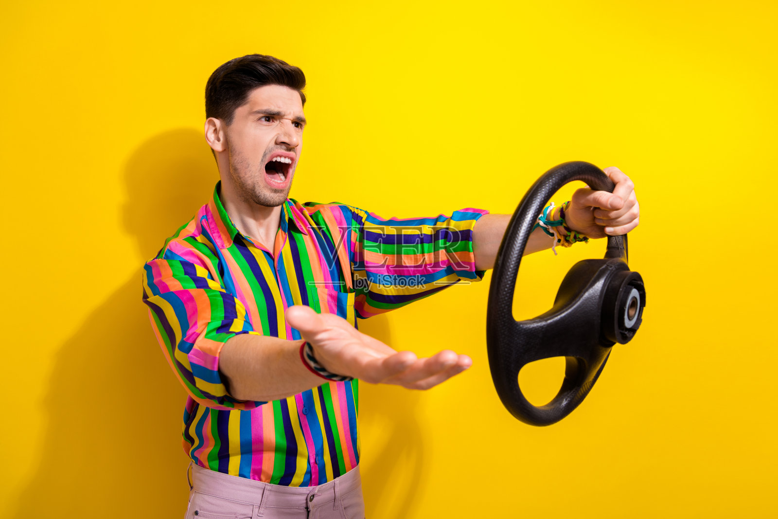 年轻愤怒的男子司机在汽车中争吵，交通堵塞，缓慢的交通堵塞方向盘模拟器孤立的黄色背景照片摄影图片