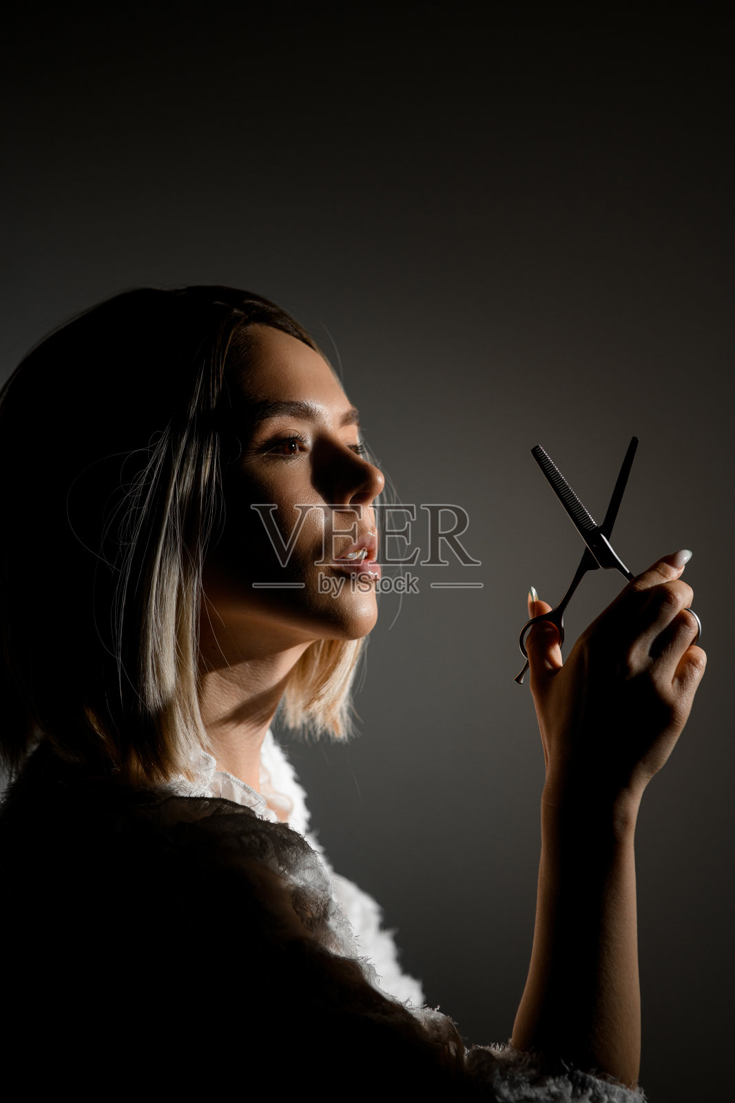 年轻美丽的美发师手持专业剪刀在背光孤立的背景，工作室拍摄照片摄影图片