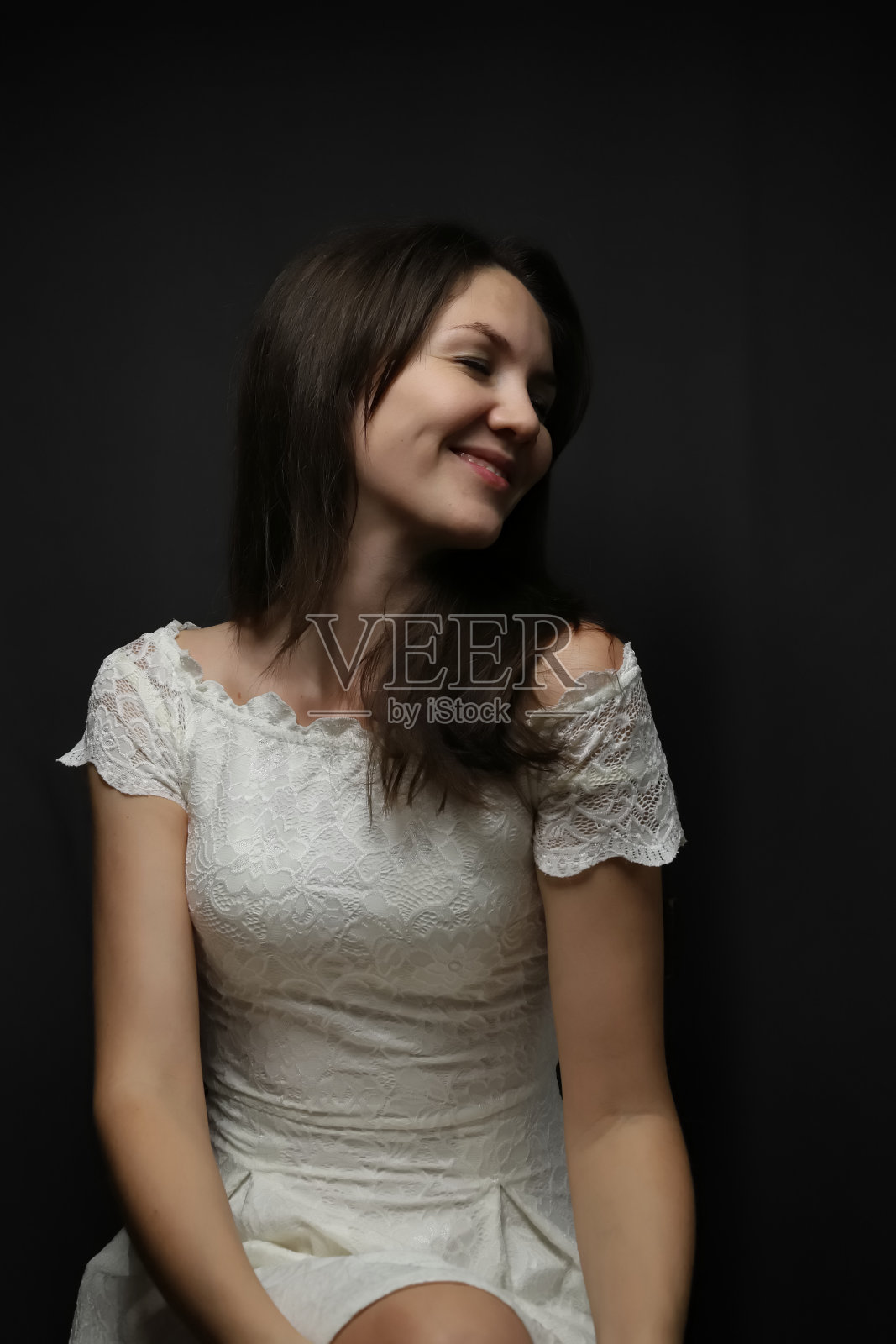 穿着黑色背景的白色连衣裙，微笑着谦虚的女人照片摄影图片