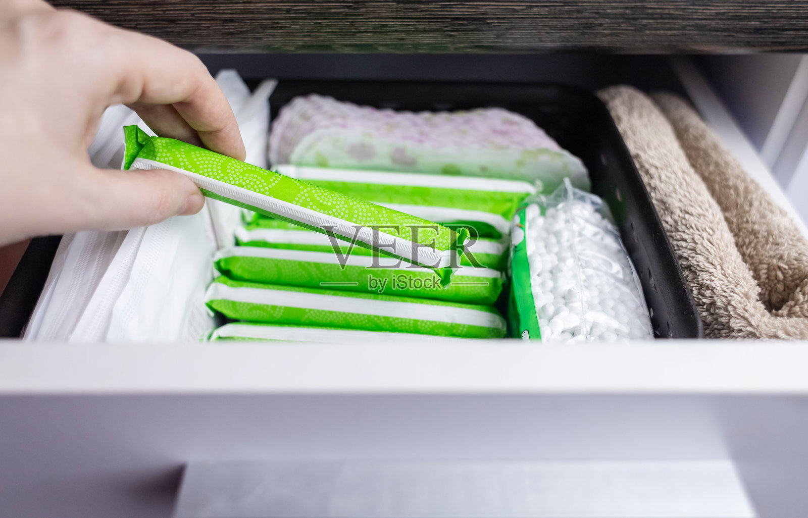 卫生巾、卫生棉条、棉花。女性把手拉出装有卫生用品的抽屉，以帮助月经。棉花花象征着没有塑料。由环保材料制成照片摄影图片