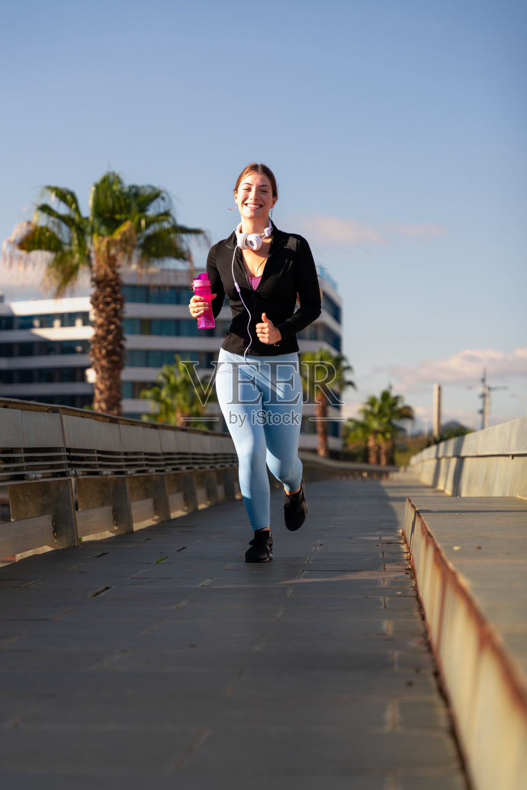 一个年轻的女人手里拿着一瓶水跑着穿过城市。照片摄影图片