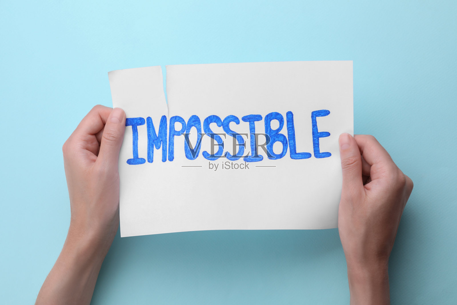 动机的概念。女人在浅蓝色背景上撕扯纸张，从“不可能”变成“可能”照片摄影图片