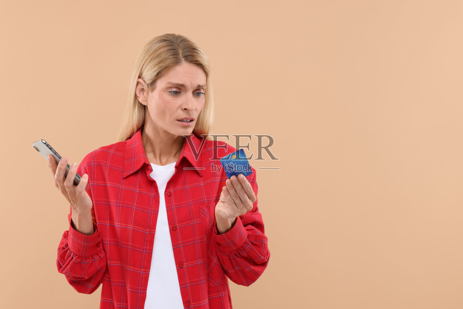 压力山大的女人把信用卡和智能手机放在米色背景上，给文字留出空间。小心-诈骗照片摄影图片