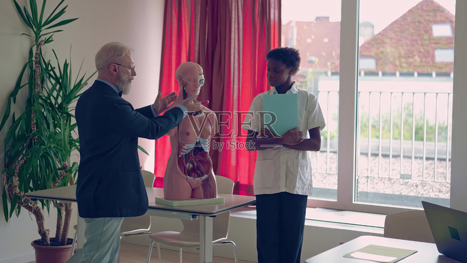 医学解剖学教授讲课解释使用人体模型与一个年轻的助手在他身边照片摄影图片