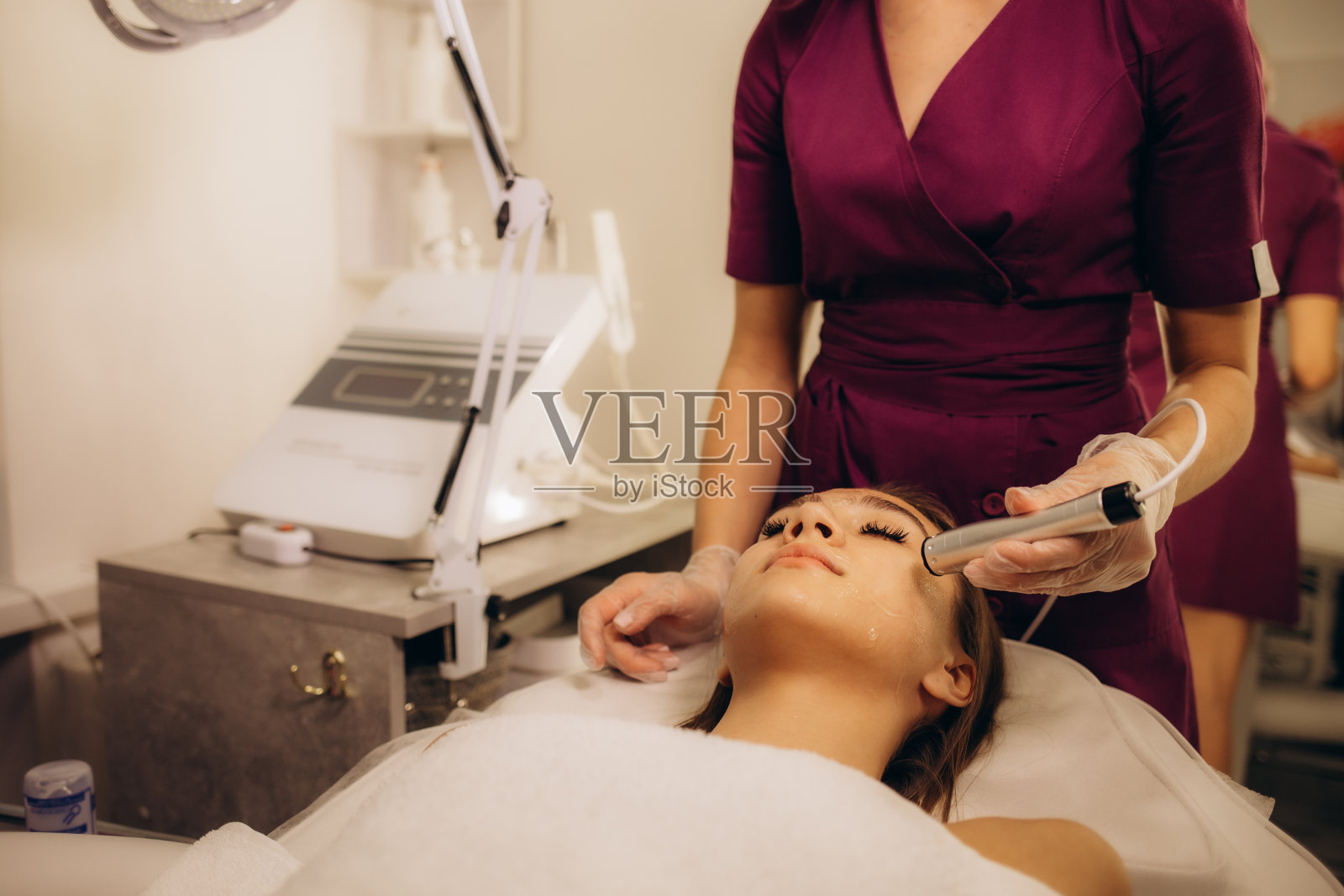 年轻白人女性接受微电流治疗。美容师的办公室。照片摄影图片