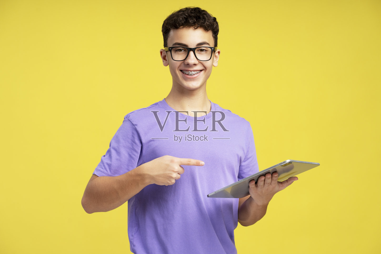 戴着时尚眼镜的微笑少年拿着平板电脑指着自己照片摄影图片