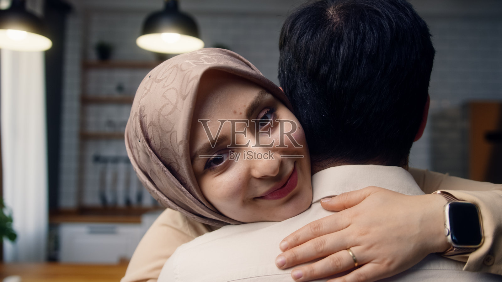 男子拥抱妻子的后视图。美丽的女人抱着她的丈夫看着镜头。近距离拥抱着一对相爱的年轻夫妇照片摄影图片