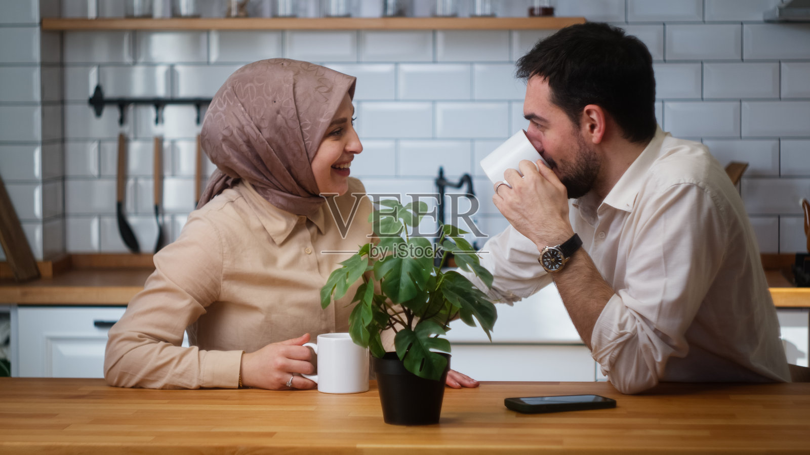 一对微笑的夫妇坐在厨房里，用杯子喝着咖啡，愉快地交谈着照片摄影图片