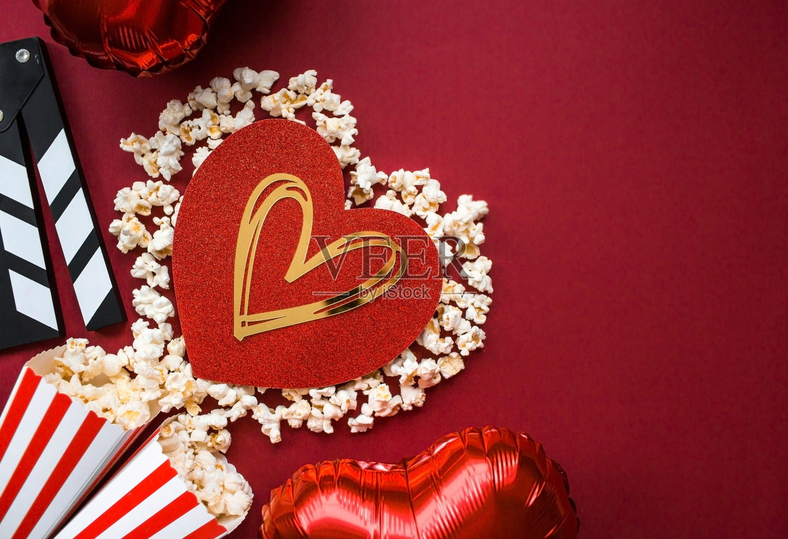 电影工业的一面旗帜。一次浪漫的电影约会。电影摄影机、3D眼镜、爆米花和红色背景上的爆米花心。这部电影将在情人节首映。照片摄影图片