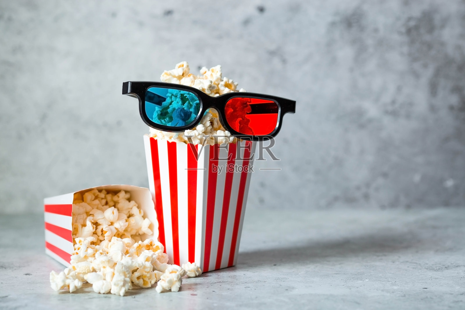 电影工业的一面旗帜。电影的上映日期。3D眼镜和爆米花装在条纹杯里，时尚的混凝土灰色背景。这部电影的首映。照片摄影图片
