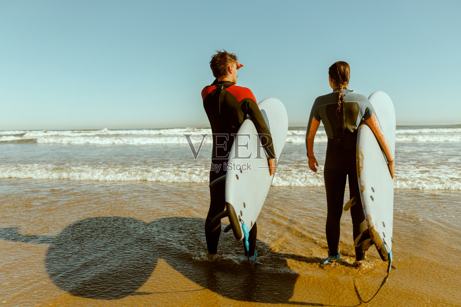 冲浪者带着冲浪板进入海洋的后视图，在波浪上冲浪照片摄影图片