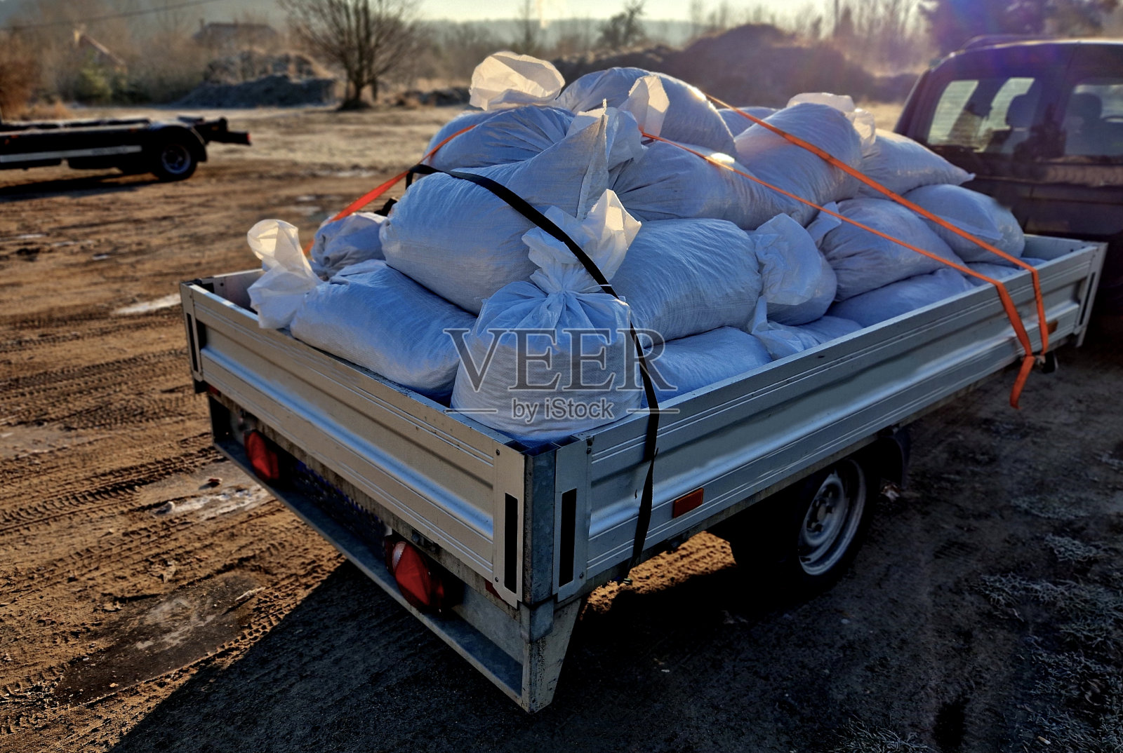汽车后面的小拖车装了很多袋子的材料。超载的升降机会被警方截停，并因超过车辆及载物的容许重量而被罚款。用带子捆扎照片摄影图片