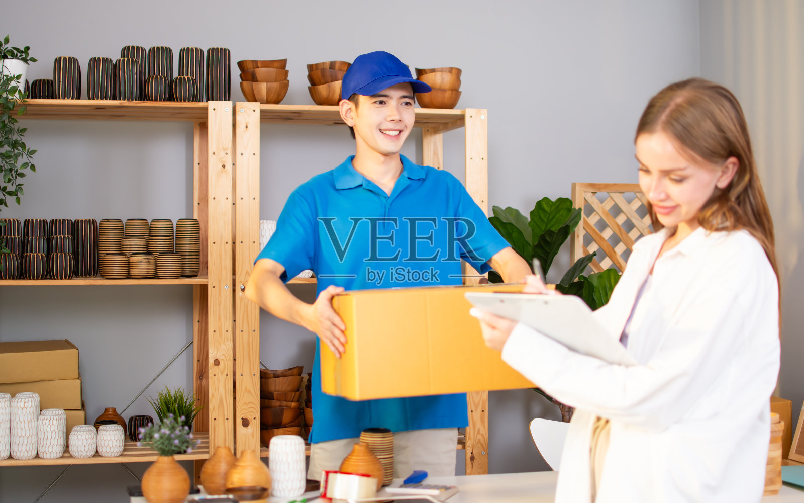 帅气的快递员穿着制服，把包裹邮寄到客户家里，服务质量很好，拿着卡盒，站在一起，微笑着，幸福地看着镜头。照片摄影图片