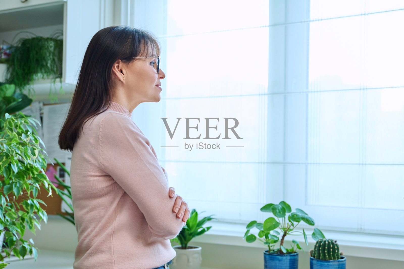 多梦的，有思想的中年妇女看着窗外的家照片摄影图片