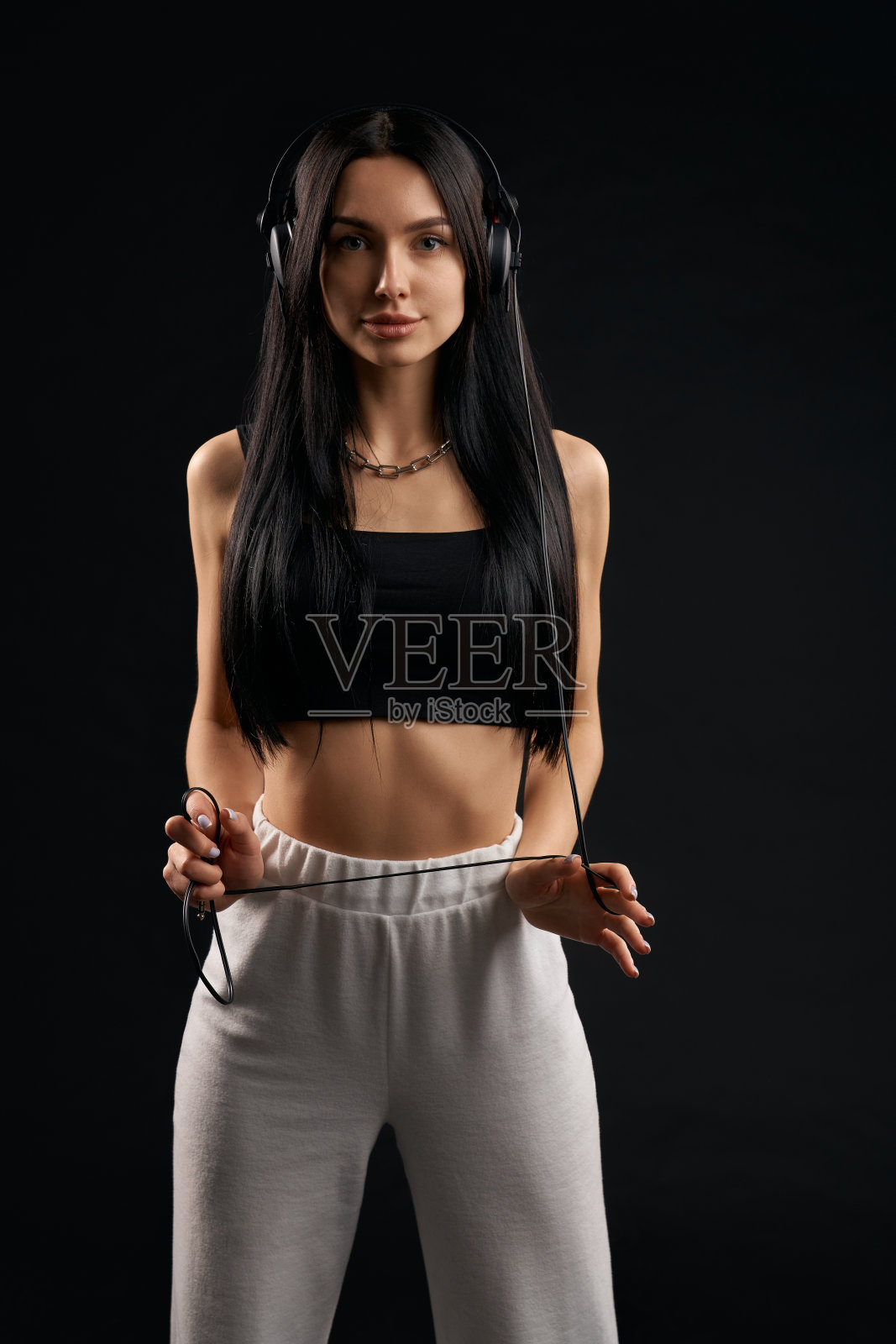 可爱的女孩穿着背心站得笔直，耳机线缠在手上。照片摄影图片