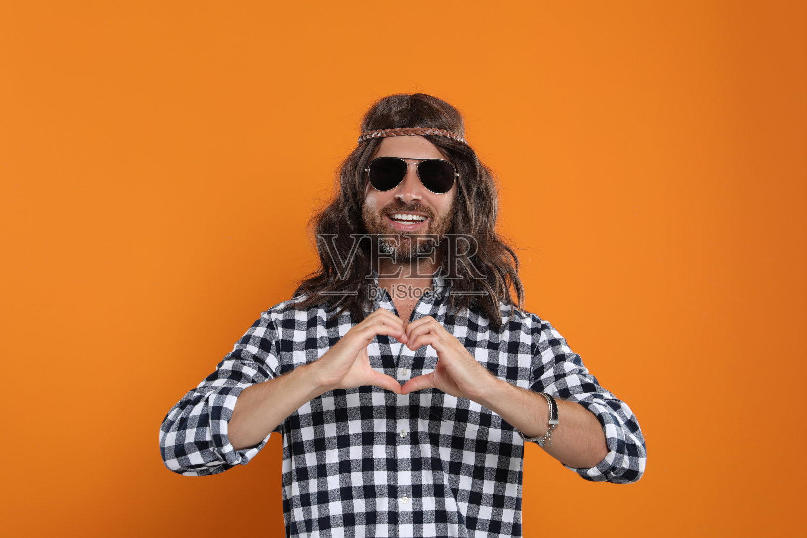戴着墨镜的嬉皮男人用手在橙色背景上做心形图案照片摄影图片