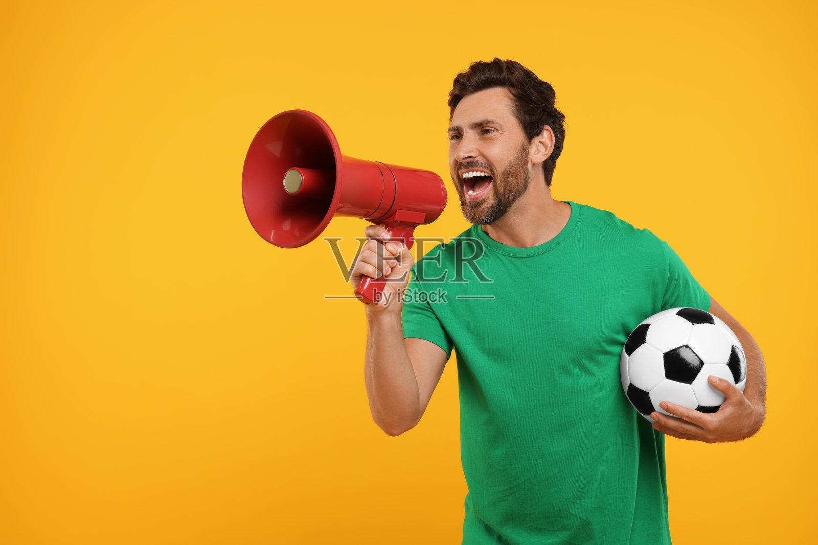 情绪化的体育迷，带着足球和橙色背景的扩音器照片摄影图片