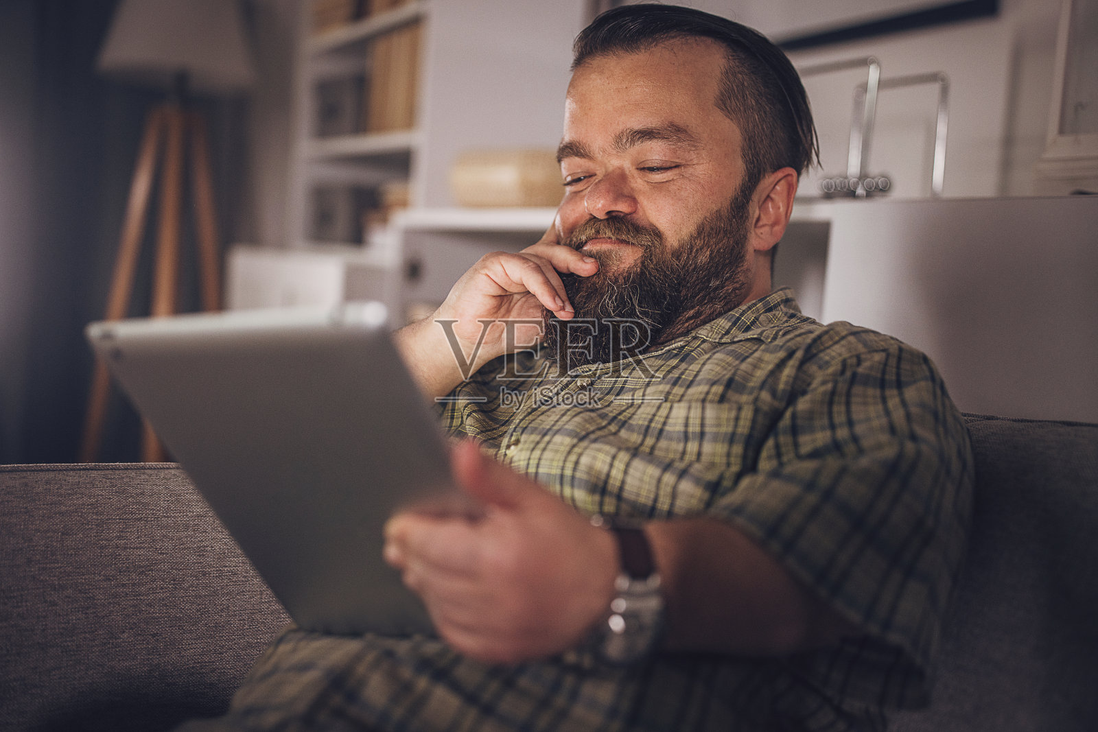 在家沙发上玩平板电脑的快乐男人照片摄影图片